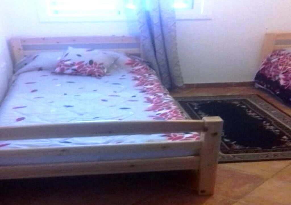 Une petite chambre avec un lit simple, un cadre en bois, une couvre-lit à motifs et un tapis foncé sur le sol.