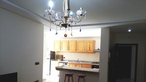 Una cocina con armarios de madera, encimera de granito y una lámpara de araña. Hay dos taburetes frente a la encimera.