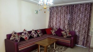 Una sala de estar con un conjunto de sofás, una mesa de centro, cortinas estampadas y una araña.