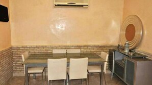 Zona pranzo con tavolo in vetro, quattro sedie, parete decorata con mattoni, condizionatore d'aria integrato e uno specchio decorativo.