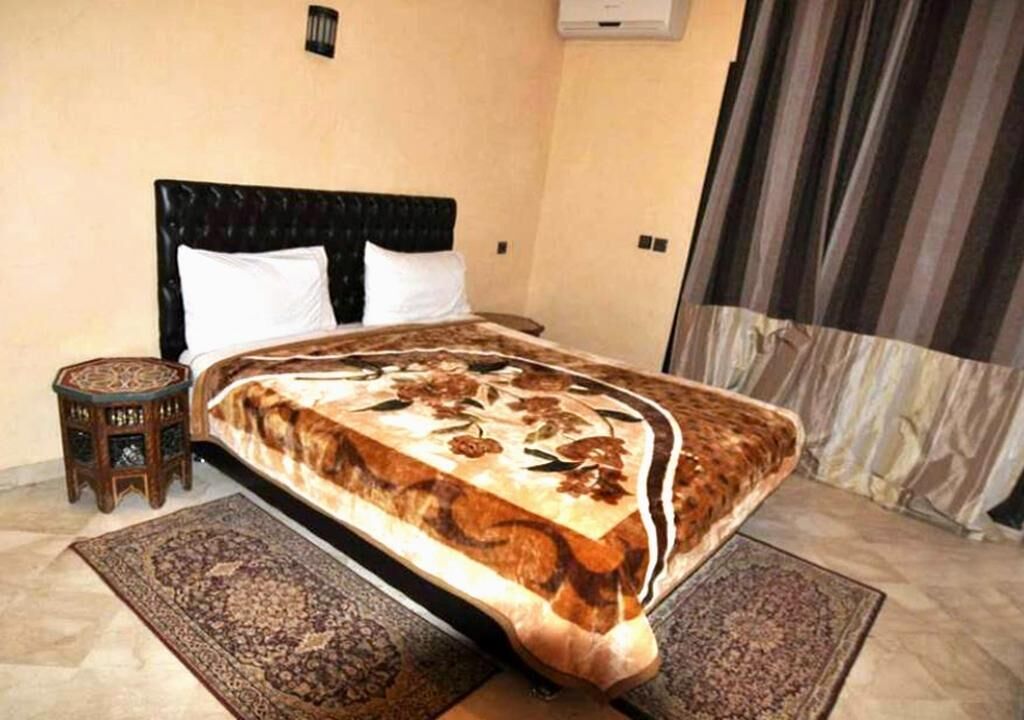 Une chambre à coucher avec un lit, une petite table de chevet et une grande fenêtre avec des rideaux.
