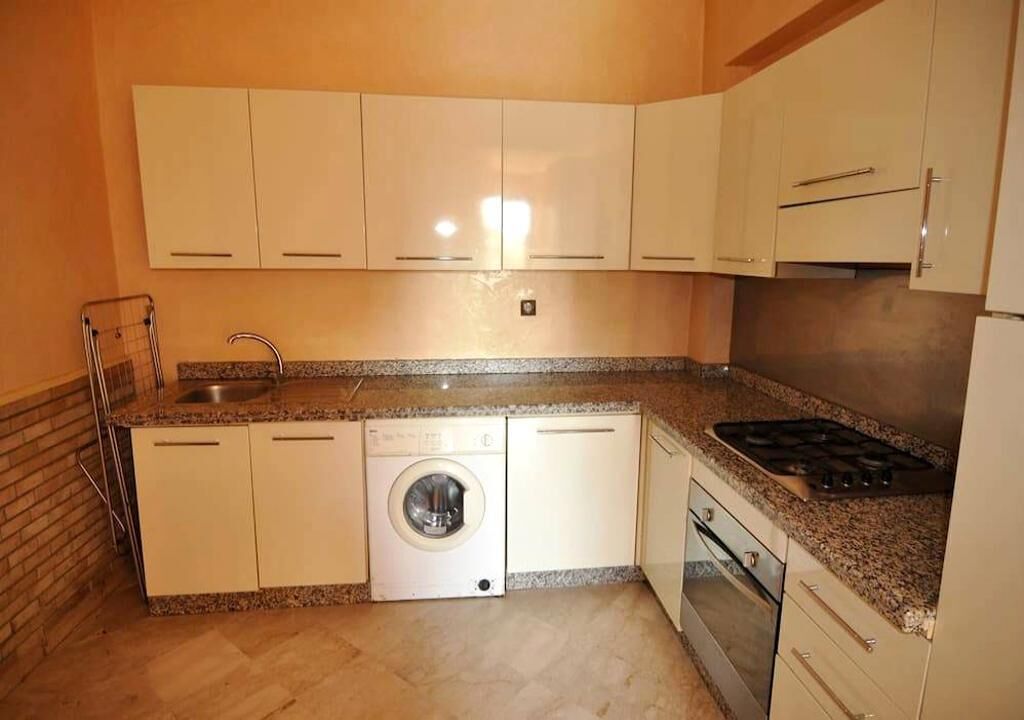 A compact kitchen with white cabinets, a washing machine, a sink, and a stove.