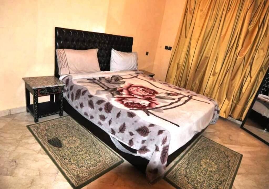 Een slaapkamer met een bed, nachtkastjes en een groot raam met gordijnen.