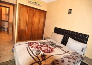 A bedroom with a bed, a wooden wardrobe, and a nightstand.