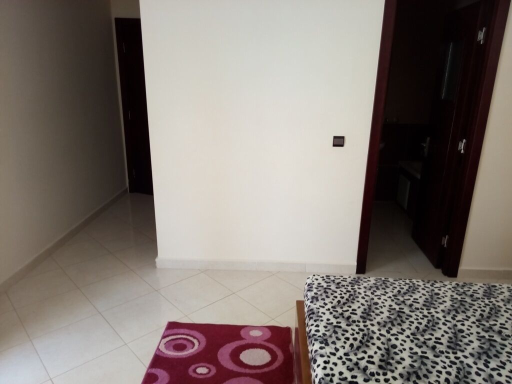 A room with a tiled floor, a bed with a patterned bedspread, and a door leading to another room.