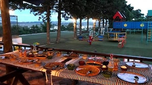 Ein Essbereich im Freien mit gedecktem Tisch, mit Blick auf einen Spielplatz und verschiedene Spielgeräte.