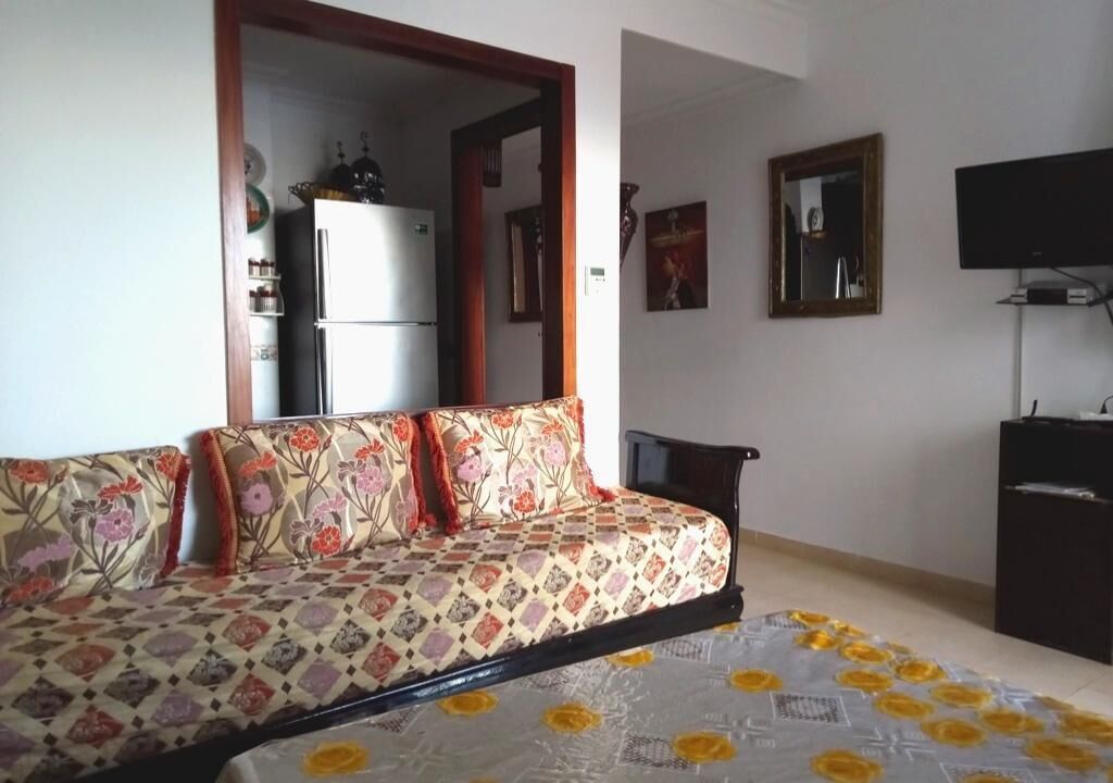 Ein Zimmer mit einer Couch, einem Fernseher, einem Kühlschrank und einem Spiegel.