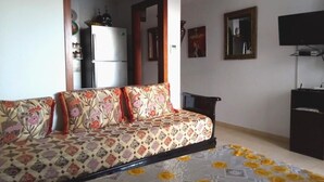 Quarto com sofá, televisão, frigorífico e espelho.