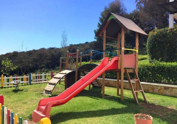 A playground with a red slide, climbing structures, and a wooden shelter.