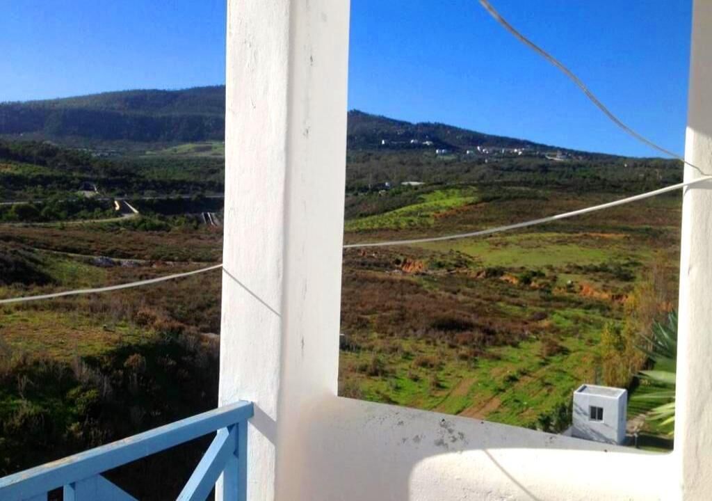 Un balcon offrant une vue sur un paysage vallonné, avec une route et des bâtiments visibles au loin.