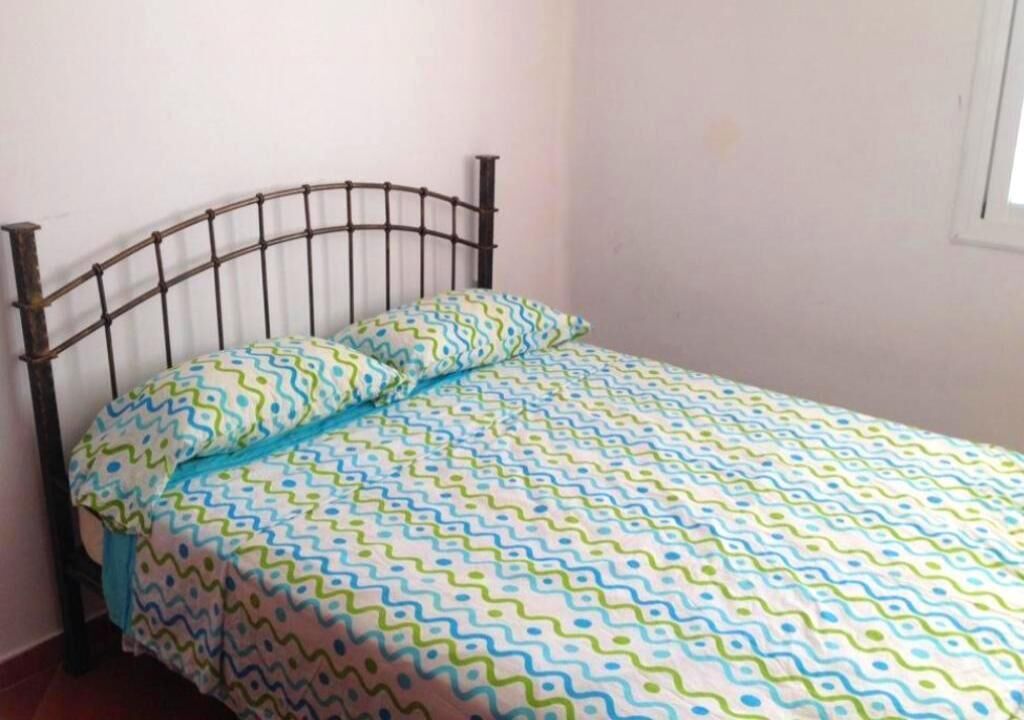 A single bed with a metal frame, a patterned bedspread, and a pillow.