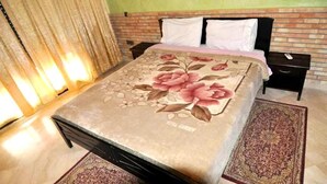 Une chambre à coucher avec une couvre-lit à motifs floraux, une tête de lit en briques, une table de chevet avec un téléphone et un tapis.