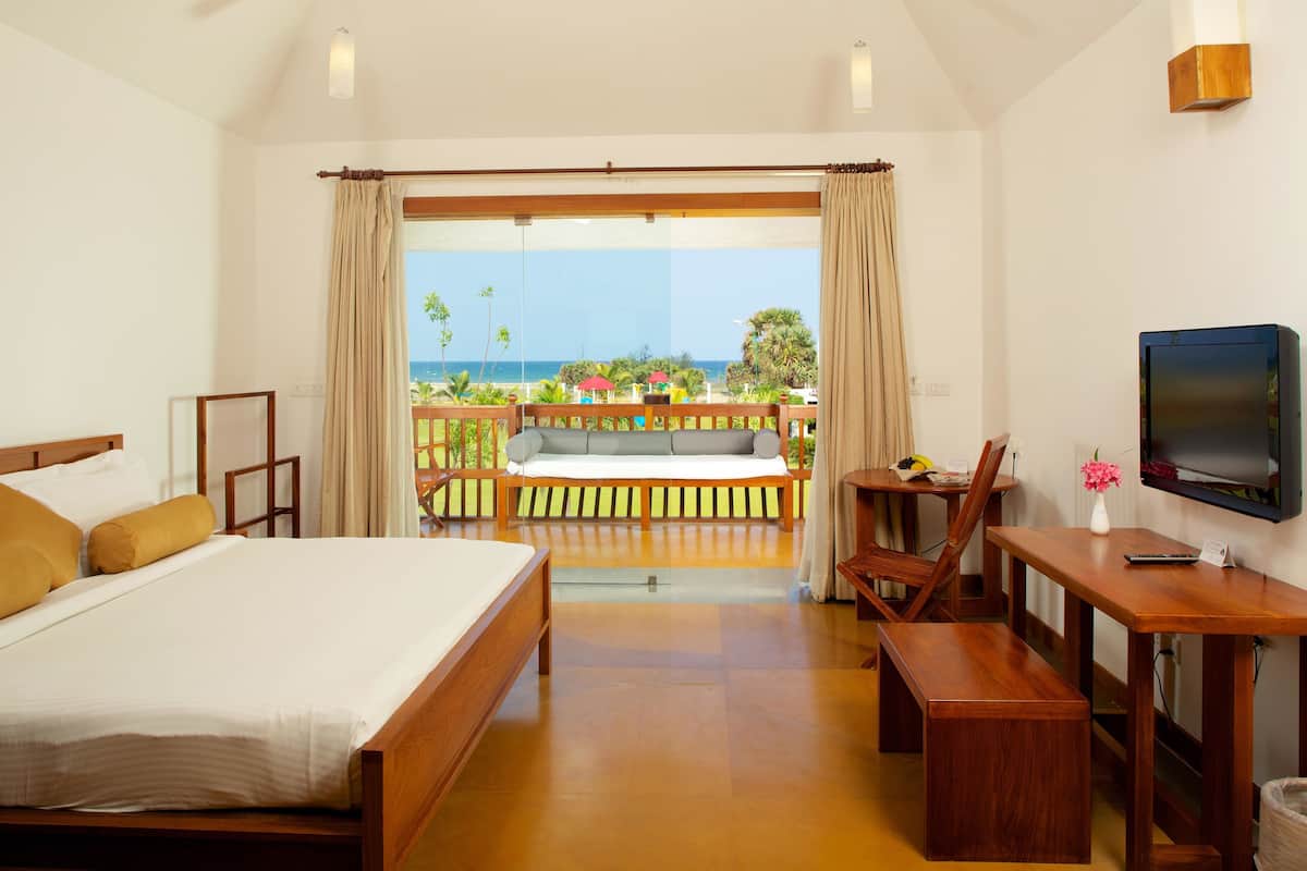 Une chambre d’hôtel avec un lit, un bureau, une télévision et un balcon donnant sur l’océan.