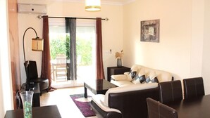Una sala de estar con un sofá, una mesa de centro y un televisor. Hay una ventana con cortinas, una lámpara y un cuadro en la pared.