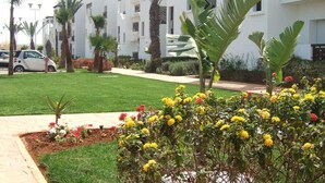 Un edificio residencial con varios balcones, un césped cuidado y una diversidad de plantas florecientes.