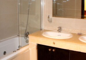 A bathroom with a bathtub, a glass-enclosed shower, and a double sink with a mirror above.
