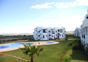 A white multi-story hotel with a swimming pool and a view of the landscape.