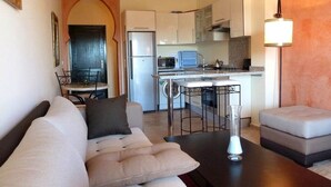 A compact living space with a sofa, a dining table, and a kitchenette. - The Greens Residence 3625 (SAIDIA)
