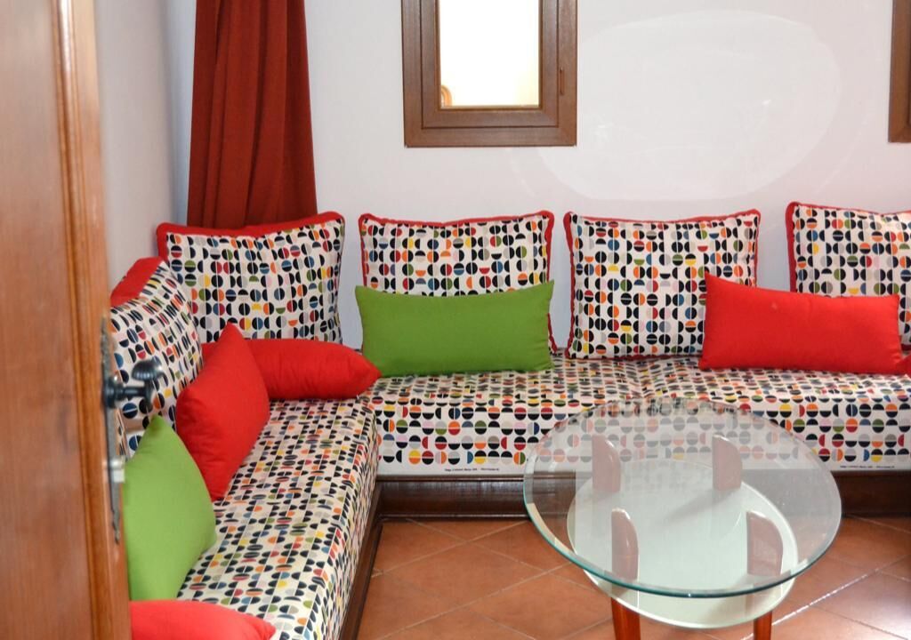 Un salon moderne avec un canapé à motifs, une table basse en verre et un rideau rouge.