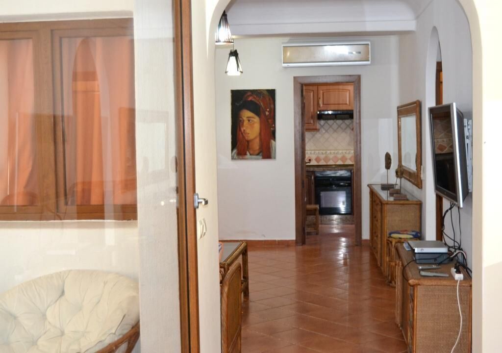 A hallway with a dining area, kitchen, and a TV on a stand.