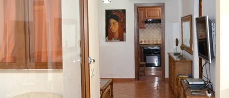 A hallway with a dining area, kitchen, and a TV on a stand.