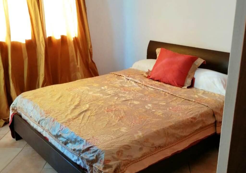 A bed with a patterned bedspread, a red pillow, and a white pillow.