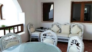 Eine Terrassenfläche mit Korbmöbeln, darunter ein runder Tisch und zwei Sofas, mit Blick ins Freie.
