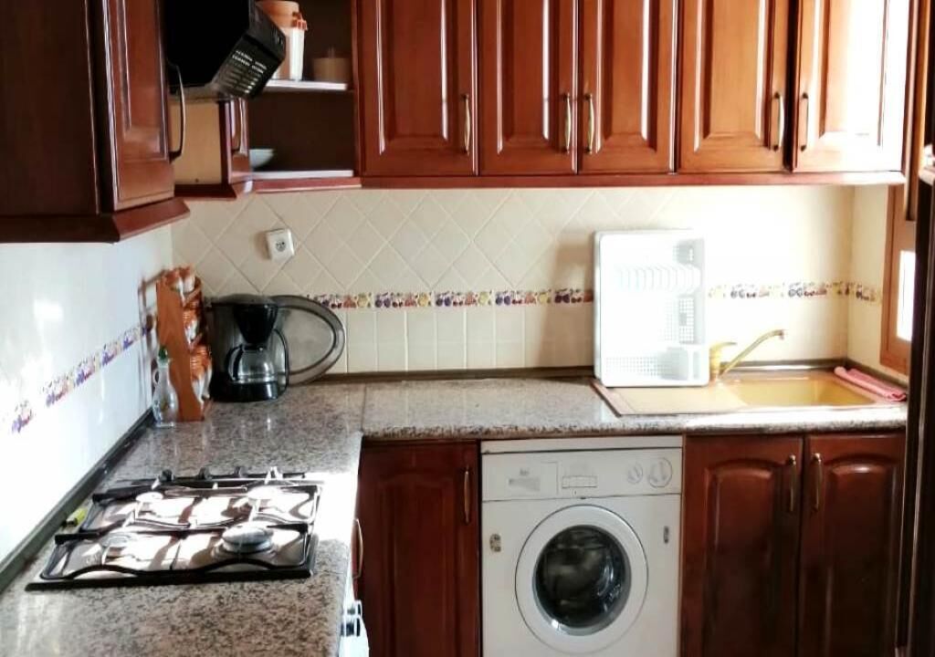 A kitchen with wooden cabinets, a microwave, a washing machine, and a coffee maker.