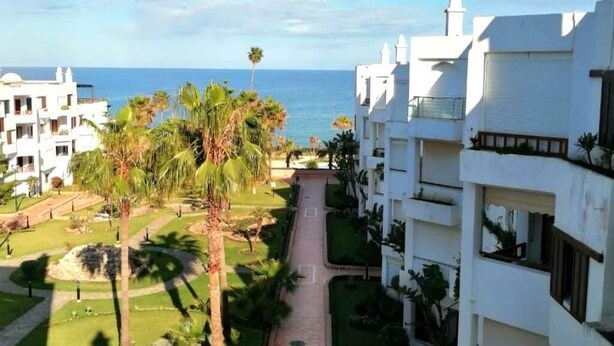 Ein Resort mit weißen Gebäuden, Palmen und Blick aufs Meer.