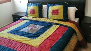 Ein Bett mit einer farbenfrohen Steude und zwei Kissen, ein schwarzes Kopfteil sowie ein kleiner Nachttisch.