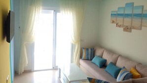 Ein Wohnzimmer mit einer Couch, einem Flachbildfernseher und einem Fenster mit Vorhängen.