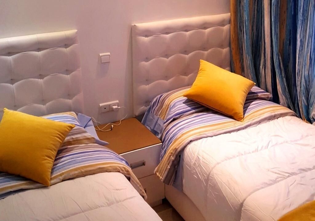 A double bed with a tufted headboard, a bedside table, and a yellow pillow.