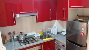Eine kleine Küche mit roten Schränken, einem Edelstahlkühlschrank, einem Gasherd, einer Spüle und einer Waschmaschine.