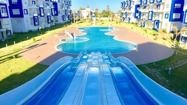 Eine Wasserrutsche, die in ein Schwimmbecken führt, umgeben von modernen Gebäuden mit Balkonen.