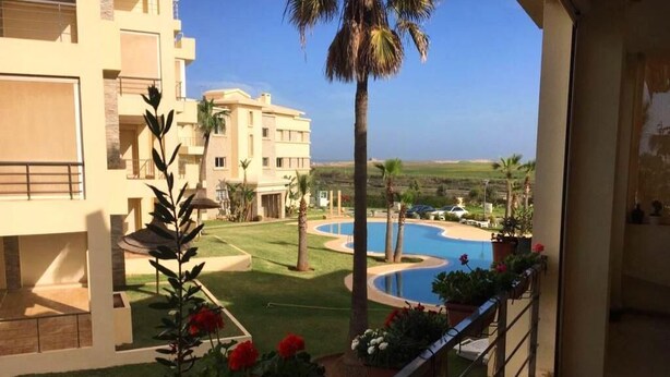 A hotel balcony with a view of a swimming pool, palm trees, and a distant landscape. - Residence Bellavis Tabznica 2432 (Bouznika)