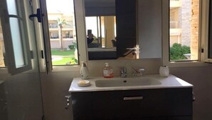 A bathroom with a sink, mirror, and toiletries. A window reveals a building and greenery outside. - Residence Bellavis Tabznica 2432 (Bouznika)