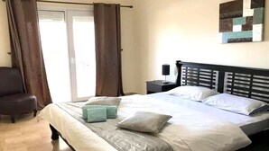 A bedroom with a bed, a chair, a nightstand, and a wall art piece.