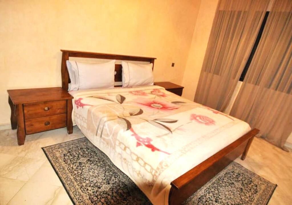A bedroom with a wooden bed, a nightstand, and a patterned rug.