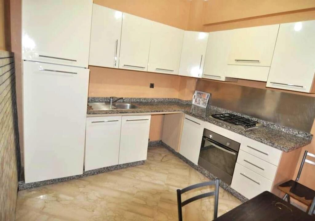 Cucina con mobili bianchi, piano di lavoro in granito, lavello in acciaio inossidabile e lavastoviglie.