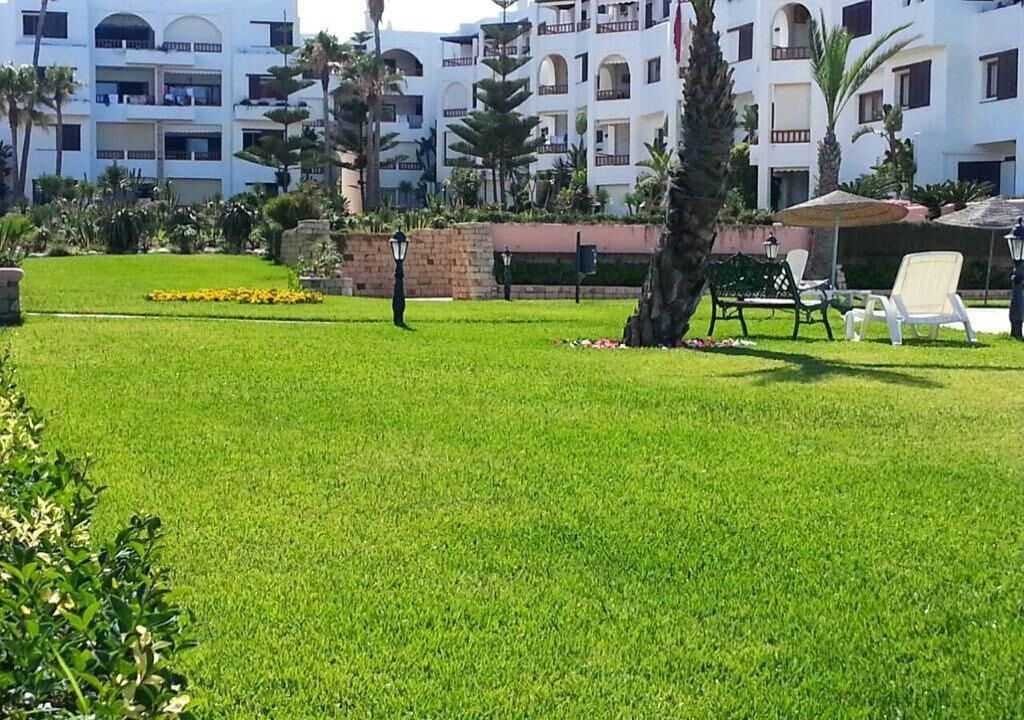A well-maintained lawn with a few chairs and a small table, surrounded by a building with balconies and a brick wall.