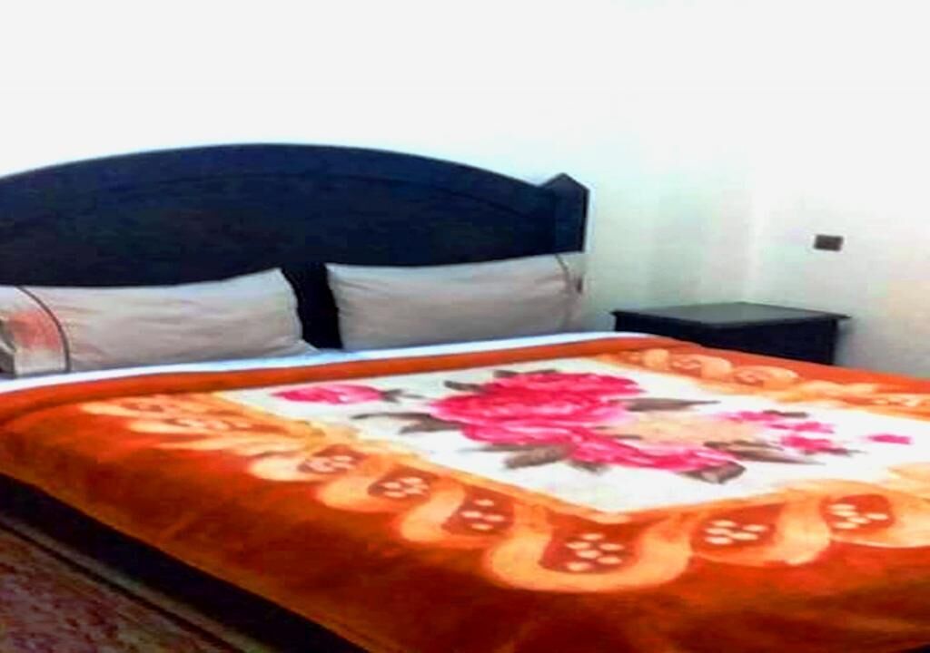 Un lit avec une couvre-lit à motifs floraux, une tête de lit sombre et une petite table de chevet.
