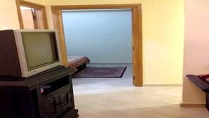 Une pièce avec un téléviseur posé sur un meuble, un lit avec un tapis, et une porte qui donne sur une autre pièce.