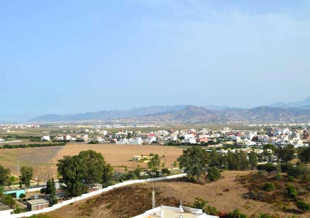 A rural town with houses and open fields, surrounded by mountains.