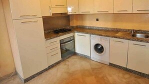 A compact kitchen with white cabinets, a built-in oven, a washing machine, and granite countertops. - Residence Babylon Marrakech 3367 (Marrakech)