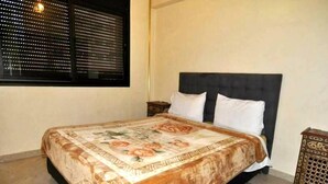 A bedroom with a bed, a window with blinds, a nightstand, and a decorative rug. - Residence Babylon Marrakech 3367 (Marrakech)