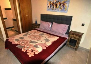 A bedroom with a bed, a nightstand, a decorative pillow, a wall painting, and a door.