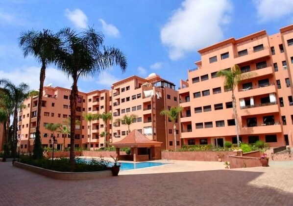 A multi-story hotel with a central courtyard, palm trees, and a swimming pool.