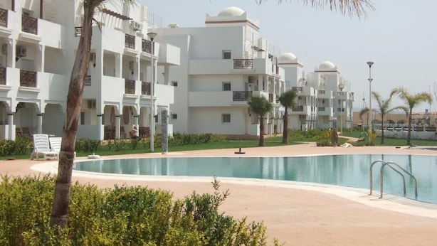Un complex turístic amb edificis blancs, una piscina i palmeres.