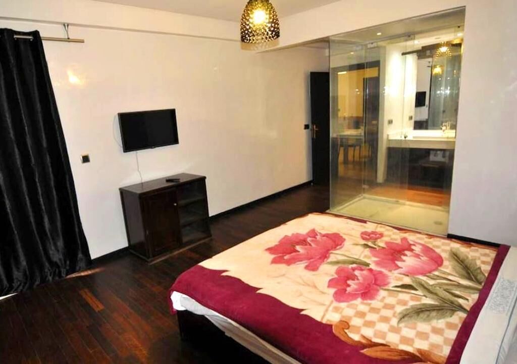 A bedroom with a bed, a television, a wardrobe, and a glass door leading to a bathroom.