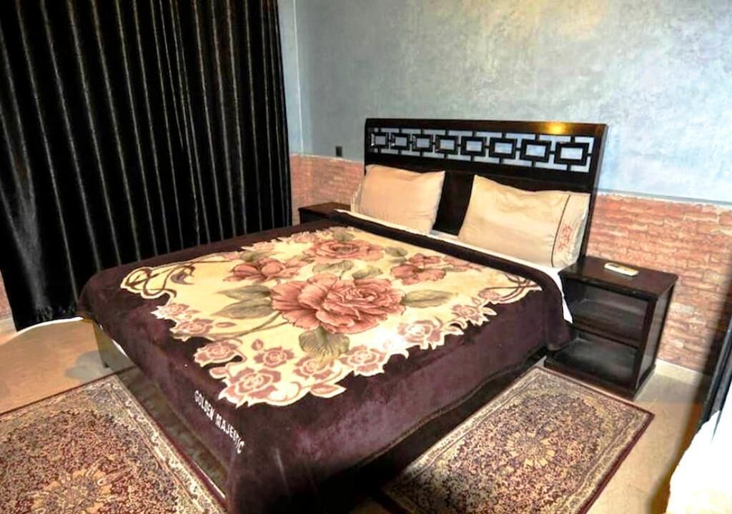 A bed with a floral bedspread, a headboard with a geometric pattern, and a nightstand with a drawer.